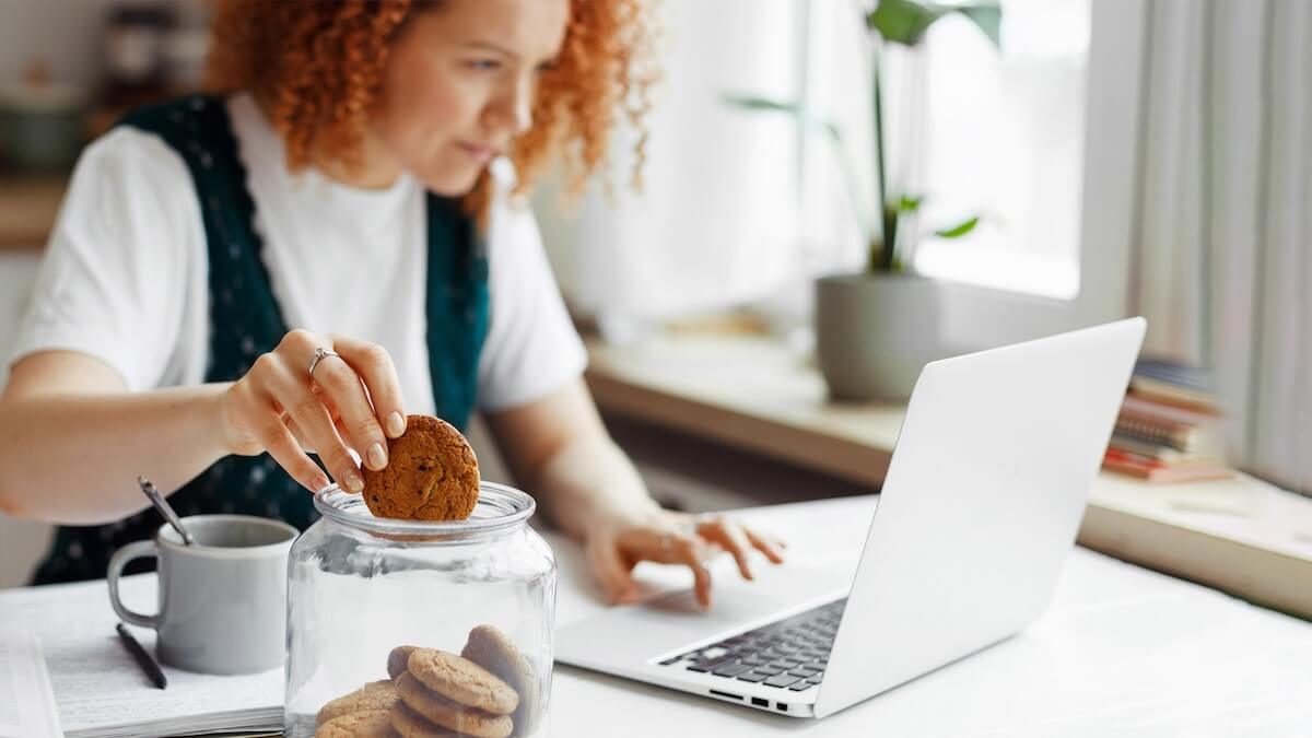 Woman working on laptop while holding a cookie